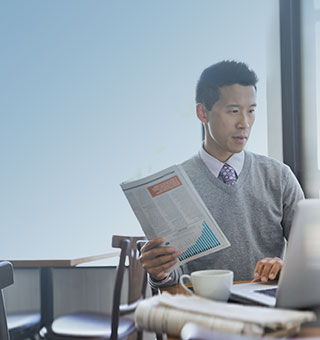 Asian guy using laptop while holding economic newspaper